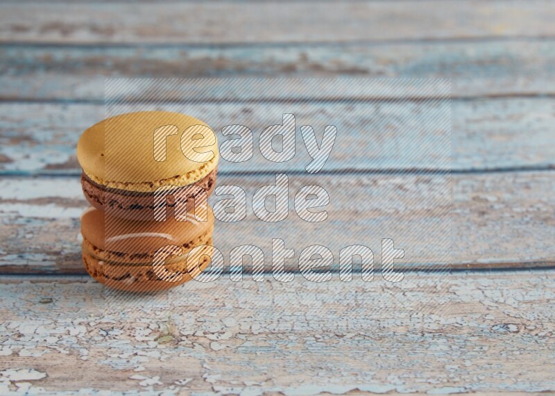 45º Shot of of two assorted Brown Irish Cream, and Yellow, and Brown Chai Latte macarons  on light blue background