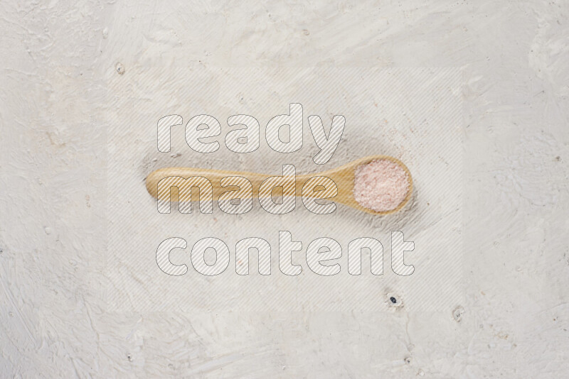 A wooden spoon full of pink himalayan salt on white background