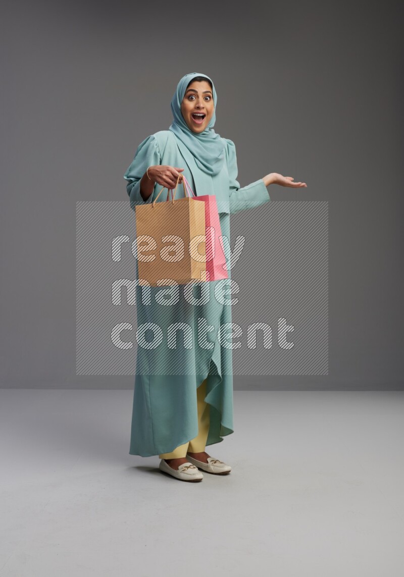 Saudi Woman wearing Abaya standing holding shopping bag on Gray background