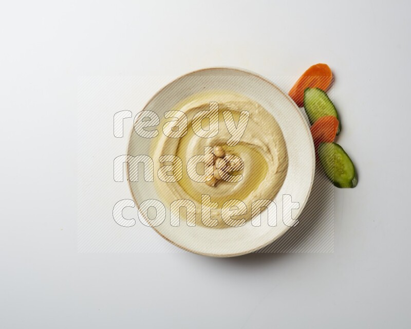 Hummus in a pottry plate garnished with roasted chickpeas on a white background
