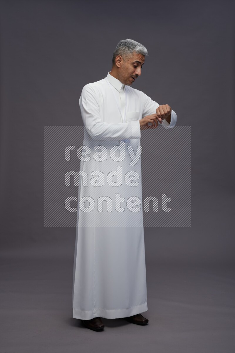 Saudi man wearing thob with neck strap employee badge standing interacting with the camera on gray background