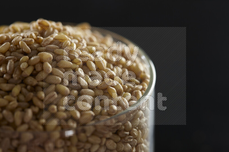 Hulled wheat in a glass jar on black background