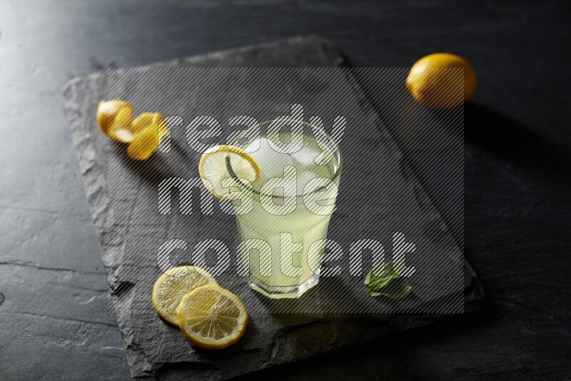 A glass of lemon juice with a lemon slice on black background