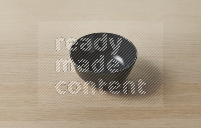 A black ceramic bowl on light wooden background