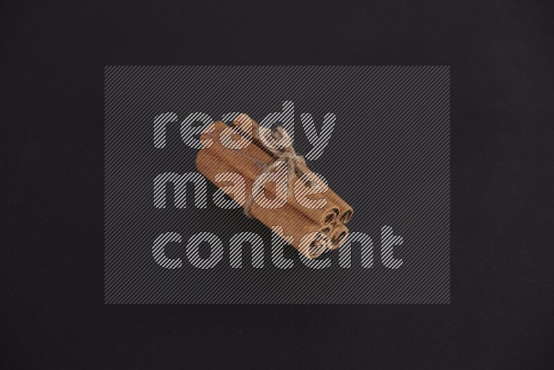 4 Cinnamon sticks stacked and bounded on black flooring