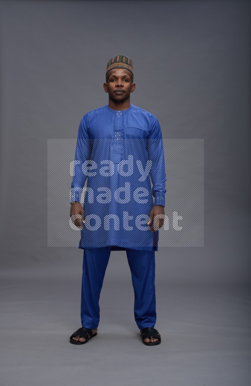 Man wearing Nigerian outfit standing interacting with the camera on gray background