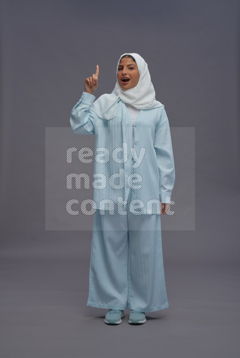 Saudi woman wearing hijab clothes standing interacting with the camera on gray background