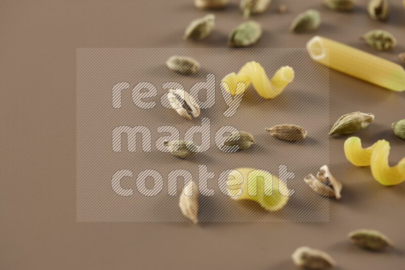 Raw pasta with different ingredients such as cherry tomatoes, garlic, onions, red chilis, black pepper, white pepper, bay laurel leaves, rosemary and cardamom on beige background