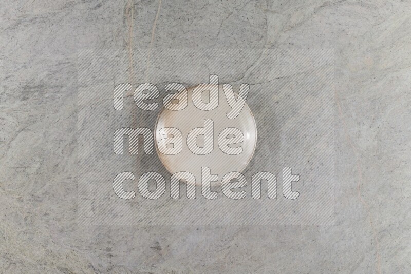 A circular beige pottery plate on grey marble background