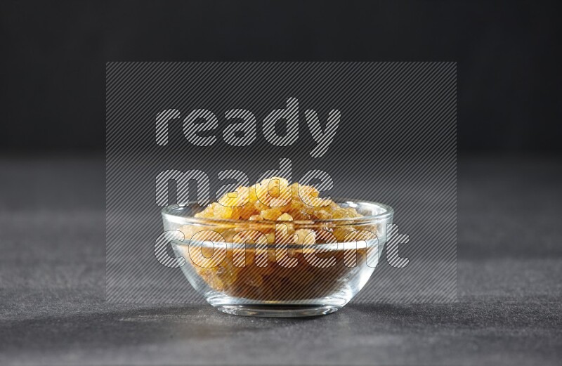 A glass bowl full of raisins on a black background in different angles