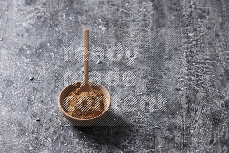 Wooden bowl full of cinnamon powder with a wooden spoon on a textured black background in different angles