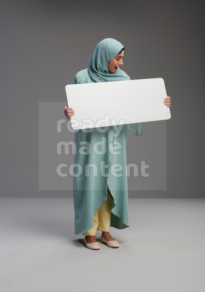 Saudi Woman wearing Abaya standing holding board on Gray background
