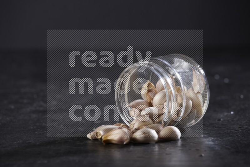 A glass jar full of garlic cloves flipped and the cloves came out on a textured black flooring