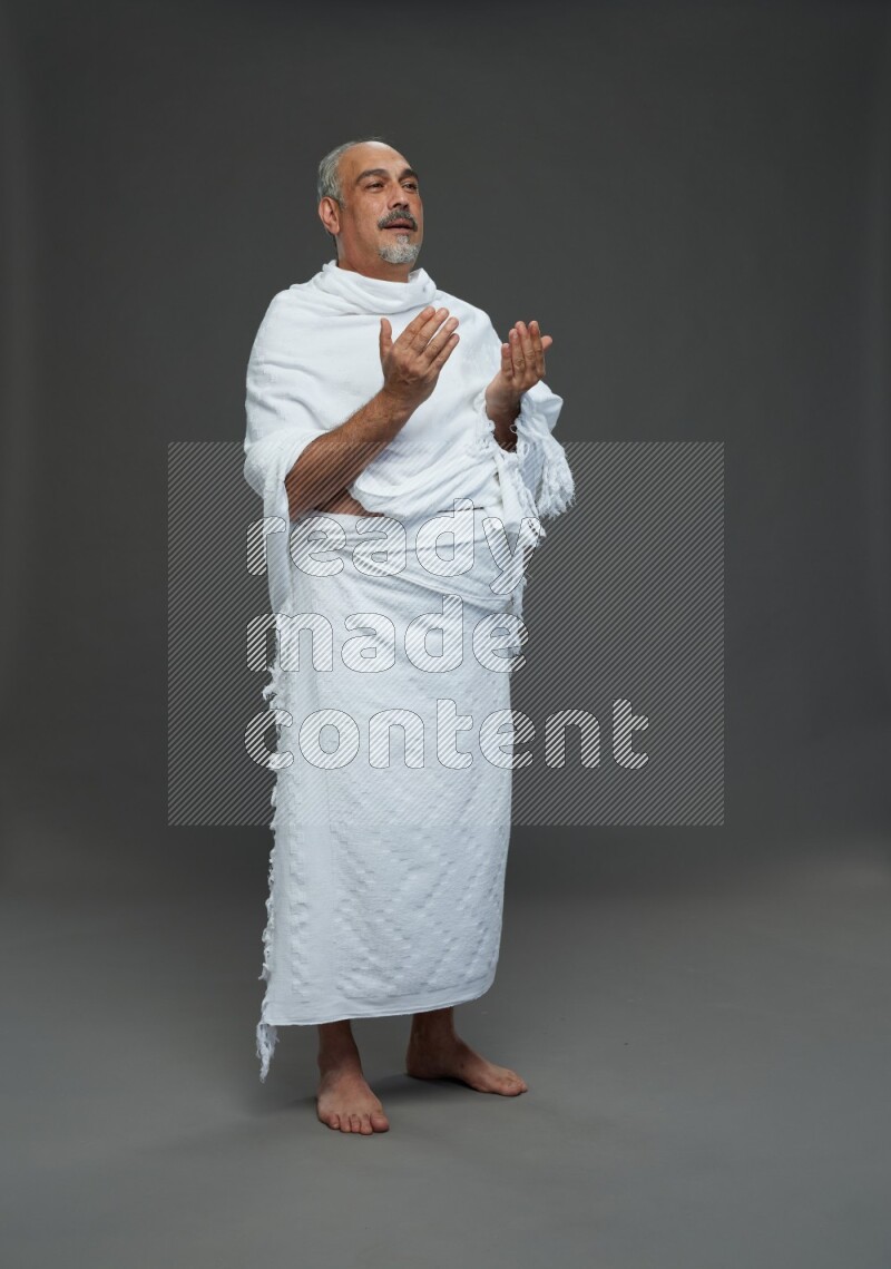 A man wearing Ehram Standing dua'a on gray background