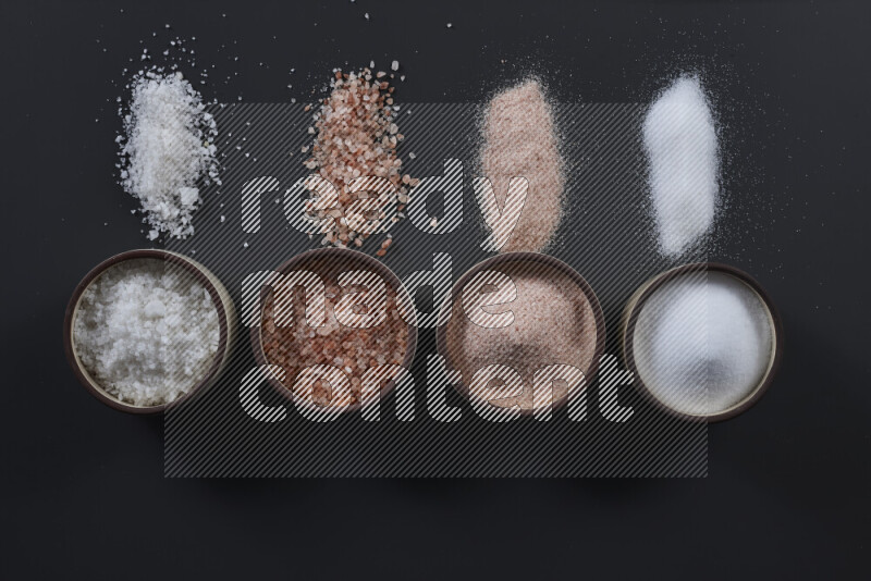 4 وعاء فخاري ممتلئين بملح الهيمالايا والملح الأبيض على خلفية سوداء