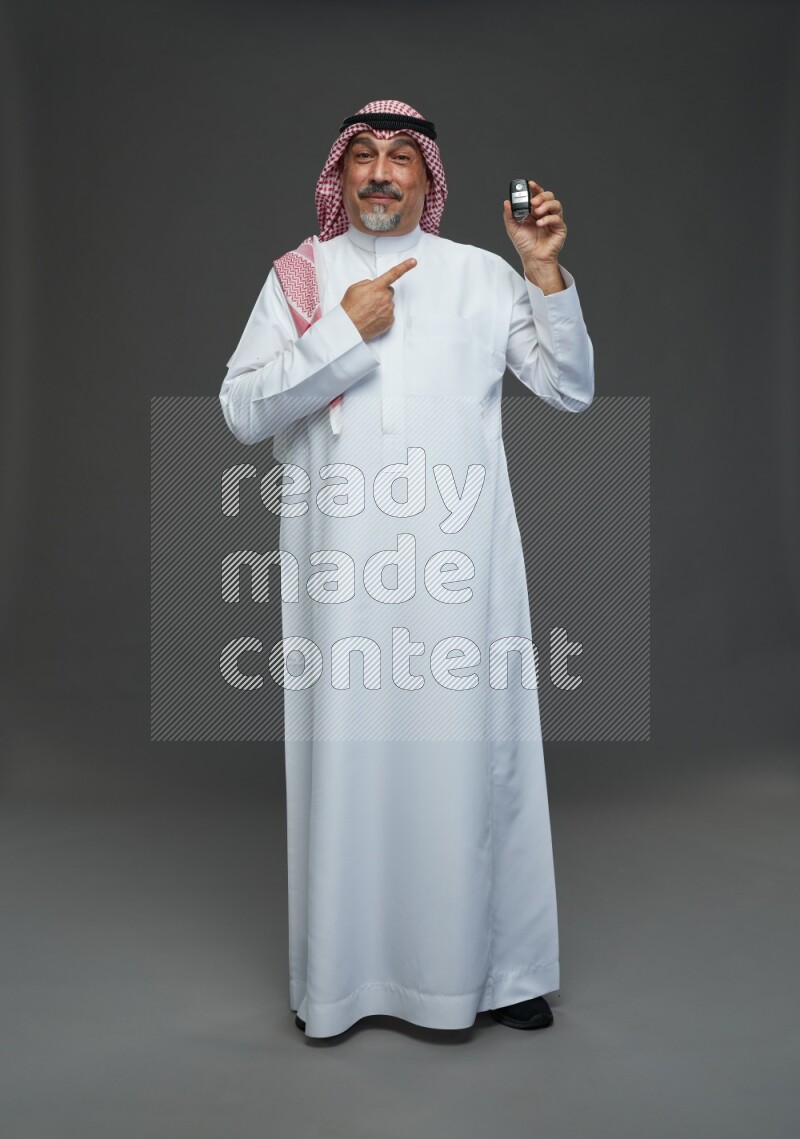 Saudi man with shomag Standing holding car key on gray background