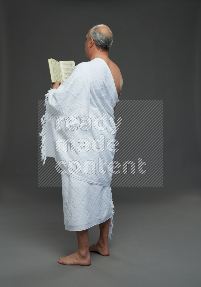 A man wearing Ehram Standing reading quran on gray background