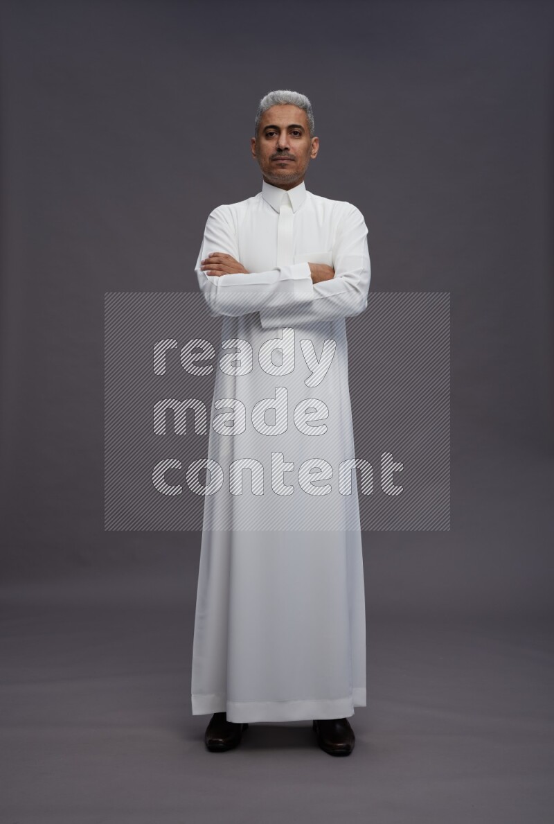 Saudi man wearing thob standing with crossed arms on gray background