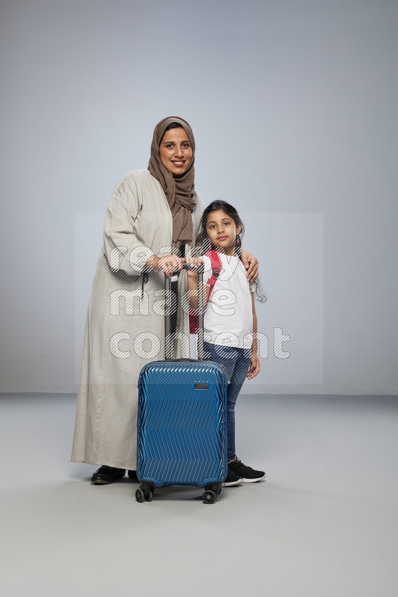 Mom and daughter standing pulling a carry-on bag on gray background