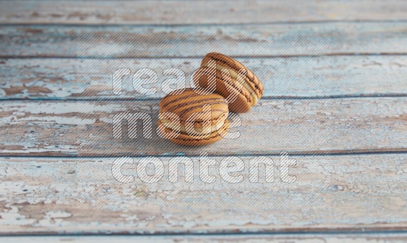 45º Shot of two light brown Almond Cream macarons on light blue wooden background