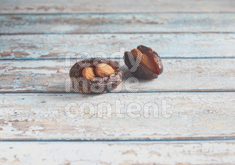 two almond stuffed madjoul dates on a light blue wooden background