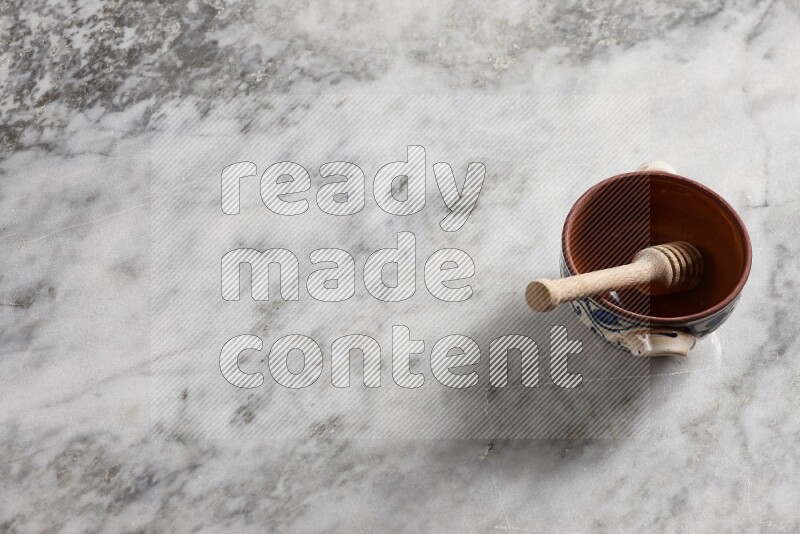 Decorative pottery pot with wooden honey dipper in it on grey marble background