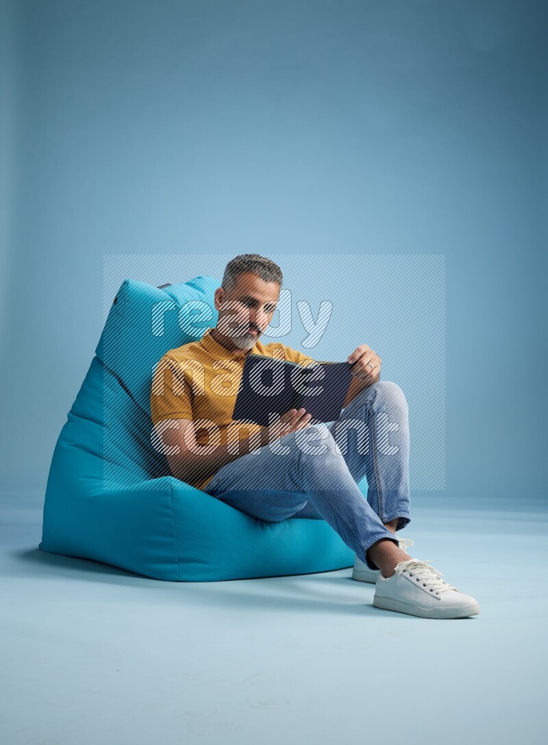 A man sitting on a blue beanbag and reading a book