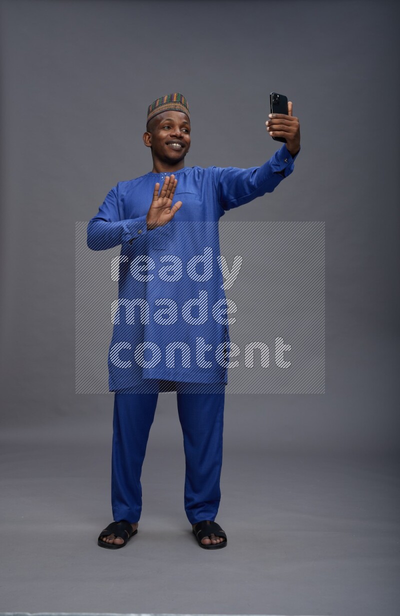 Man wearing Nigerian outfit standing taking selfie on gray background