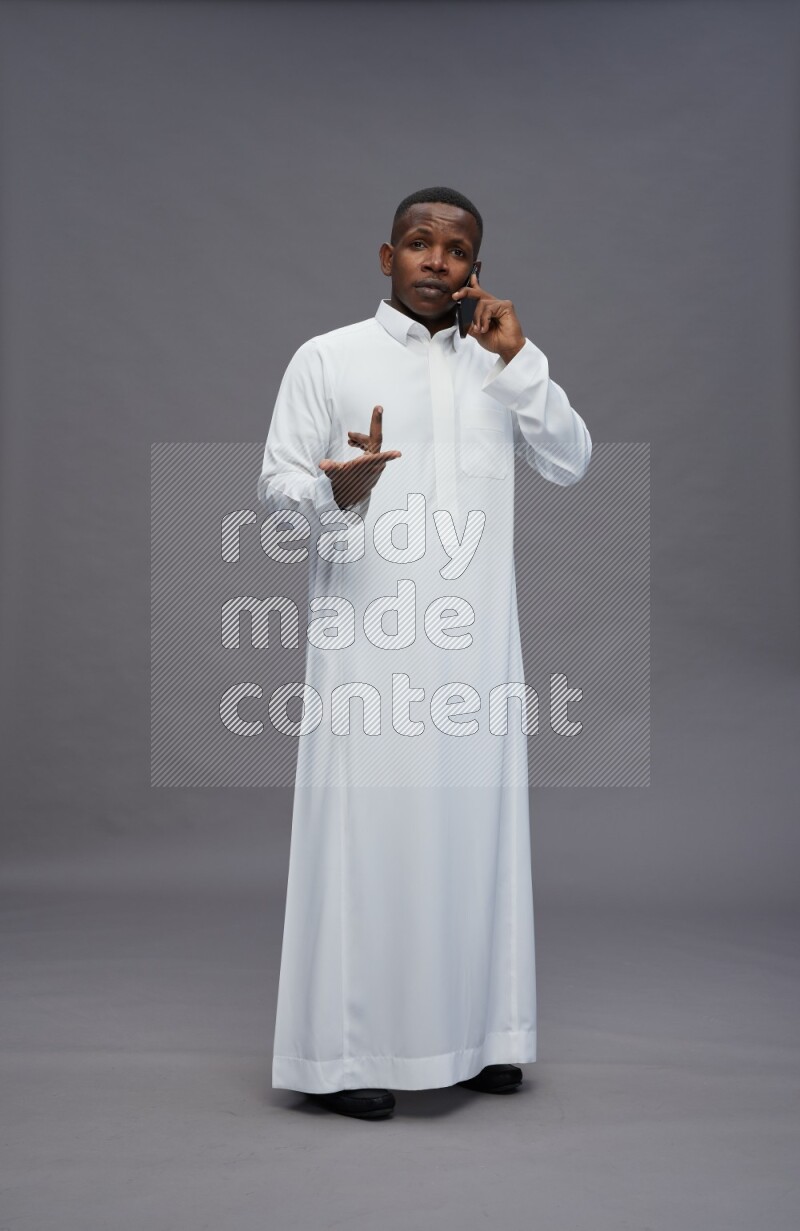 Saudi man wearing thob standing talking on phone on gray background