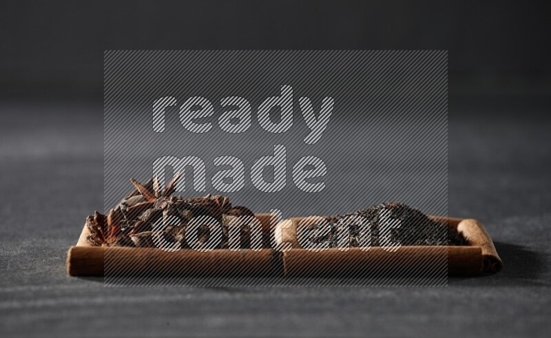 مربعان من أعواد القرفة ممتلئان باليانسون النجمي والشاي الأسود علي خلفية سوداء