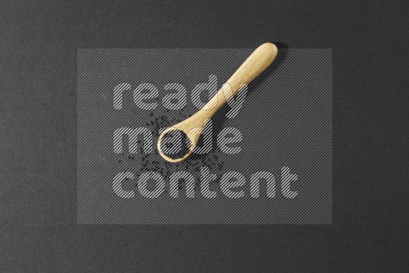 A wooden spoon full of black seeds and seeds spread beside it on a black flooring