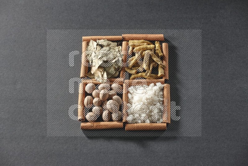 4 squares of cinnamon sticks full of bay laurel leaves, white salt, turmeric fingers and nutmegs on black flooring