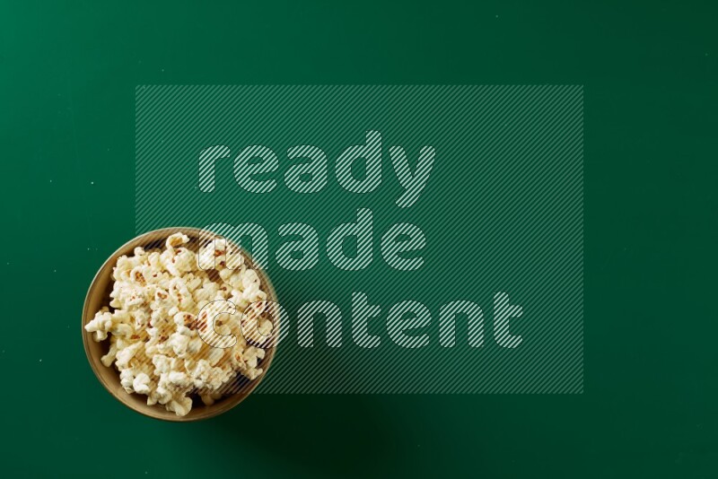 An off white ceramic bowl full of popcorn on a green background in a top view shot