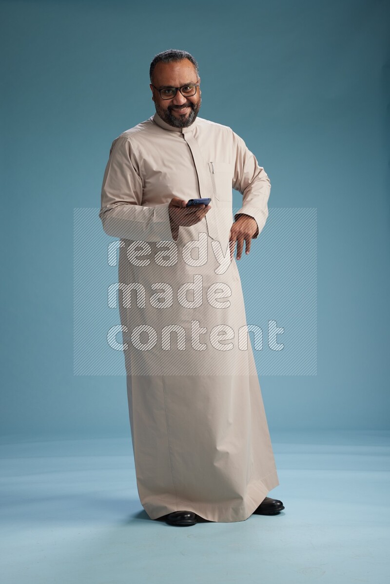 Saudi Man without shimag Standing texting on phone on blue background