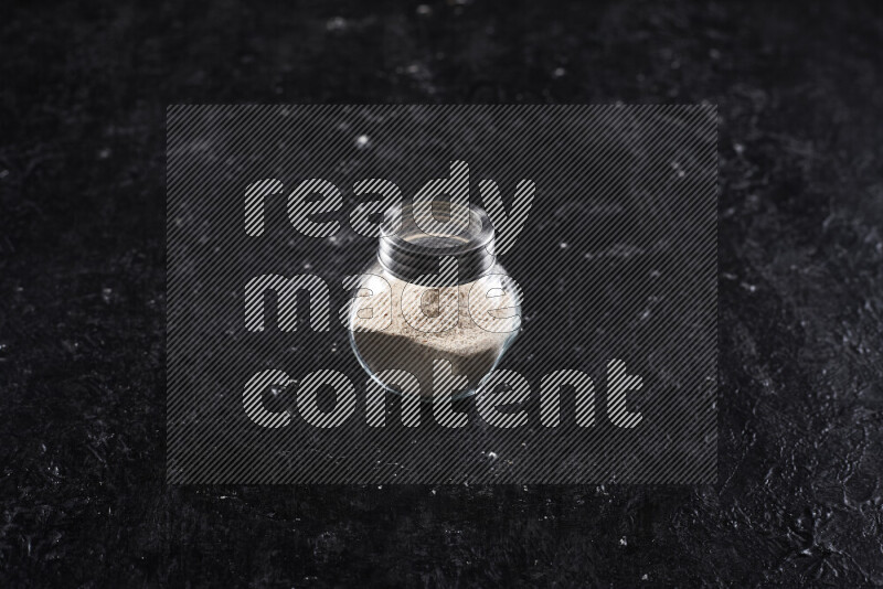 A glass jar full of onion powder on black background