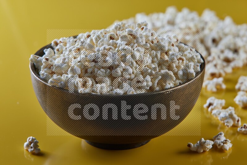 A copper ceramic bowl full of popcorn with popcorn beside it on a yellow background in different angles