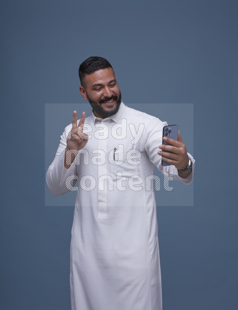 A Saudi man Taking A Selfie on Blue Background wearing Saudi Thob