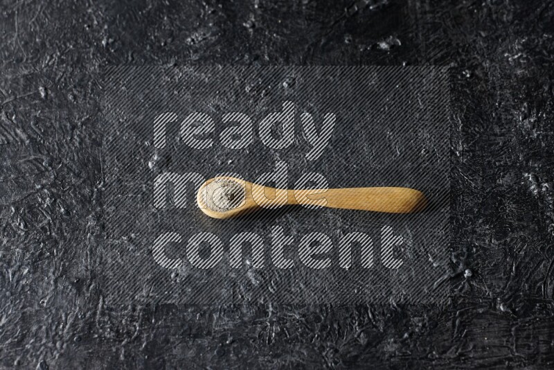 A wooden spoon full of white pepper powder on textured black flooring