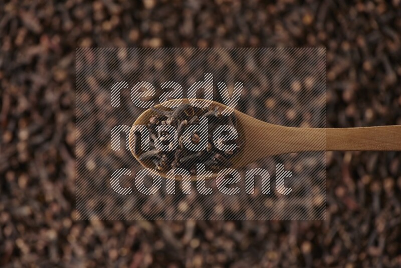 A wooden spoon full of cloves on cloves background and black flooring