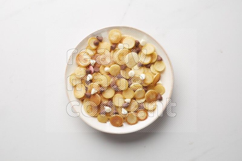 Top-view shot of mixed chocolate chips cereal pancakes in a round bowl on white background
