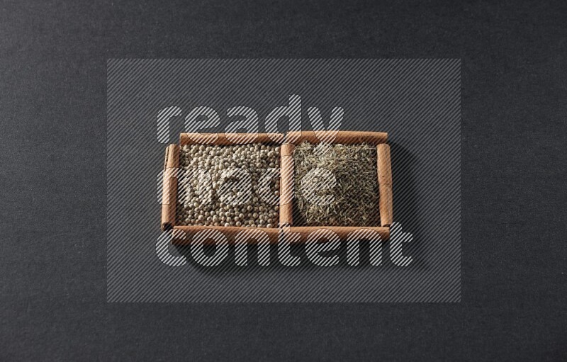 مربعان من أعواد القرفة ممتلئان بحبوب الفلفل الأبيض وحبوب الكمون علي خلفية سوداء