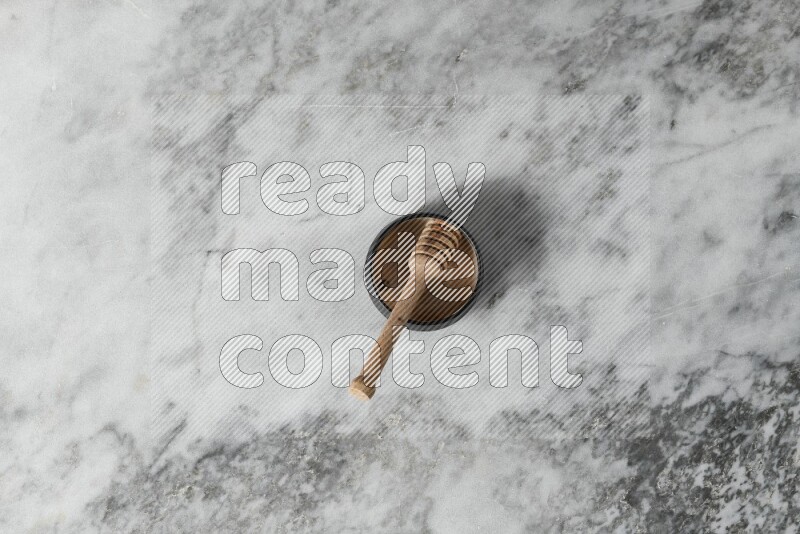 Black pottery bowl with wooden honey dipper in it on grey marble background