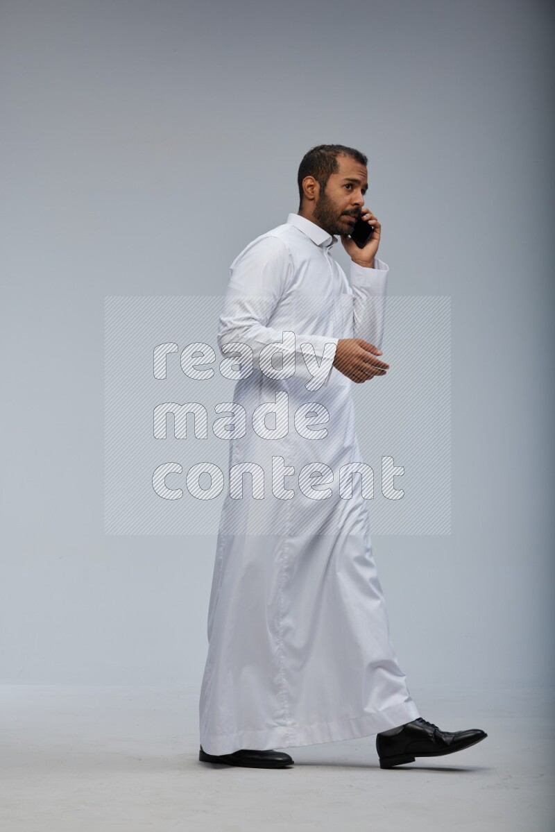 Saudi man wearing Thob standing talking on phone on Gray background