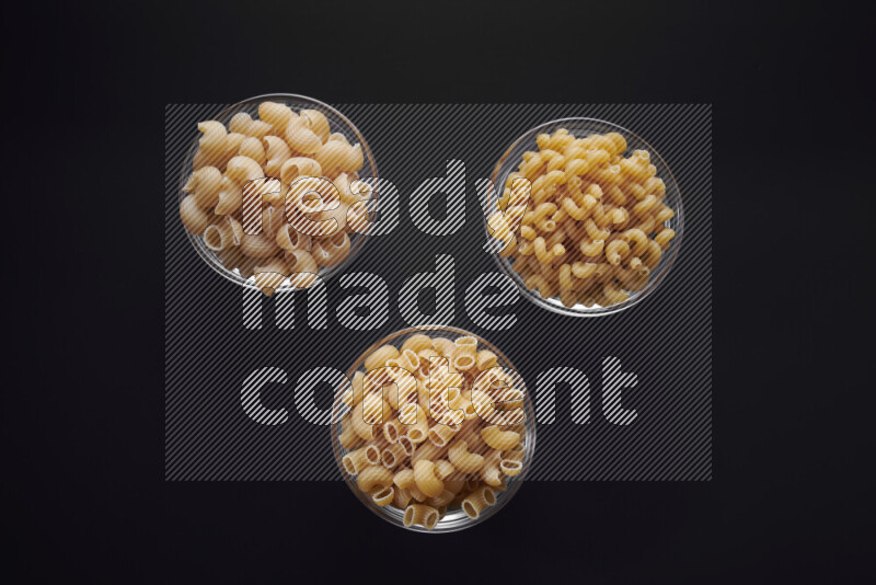 Different pasta types in glass bowls on black background