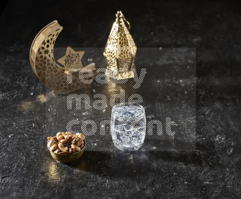 مكسرات في وعاء معدني مع كوب من الماء بجانب فوانيس ذهبية علي خلفية سوداء