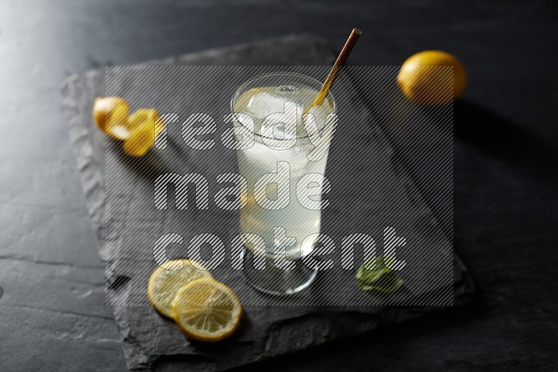 A glass of lemon juice with a straw on black background