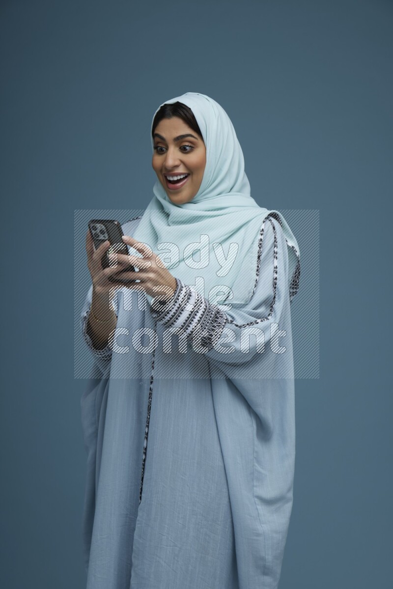 A Saudi woman Texting in a blue background wearing a blue Abaya with hijab