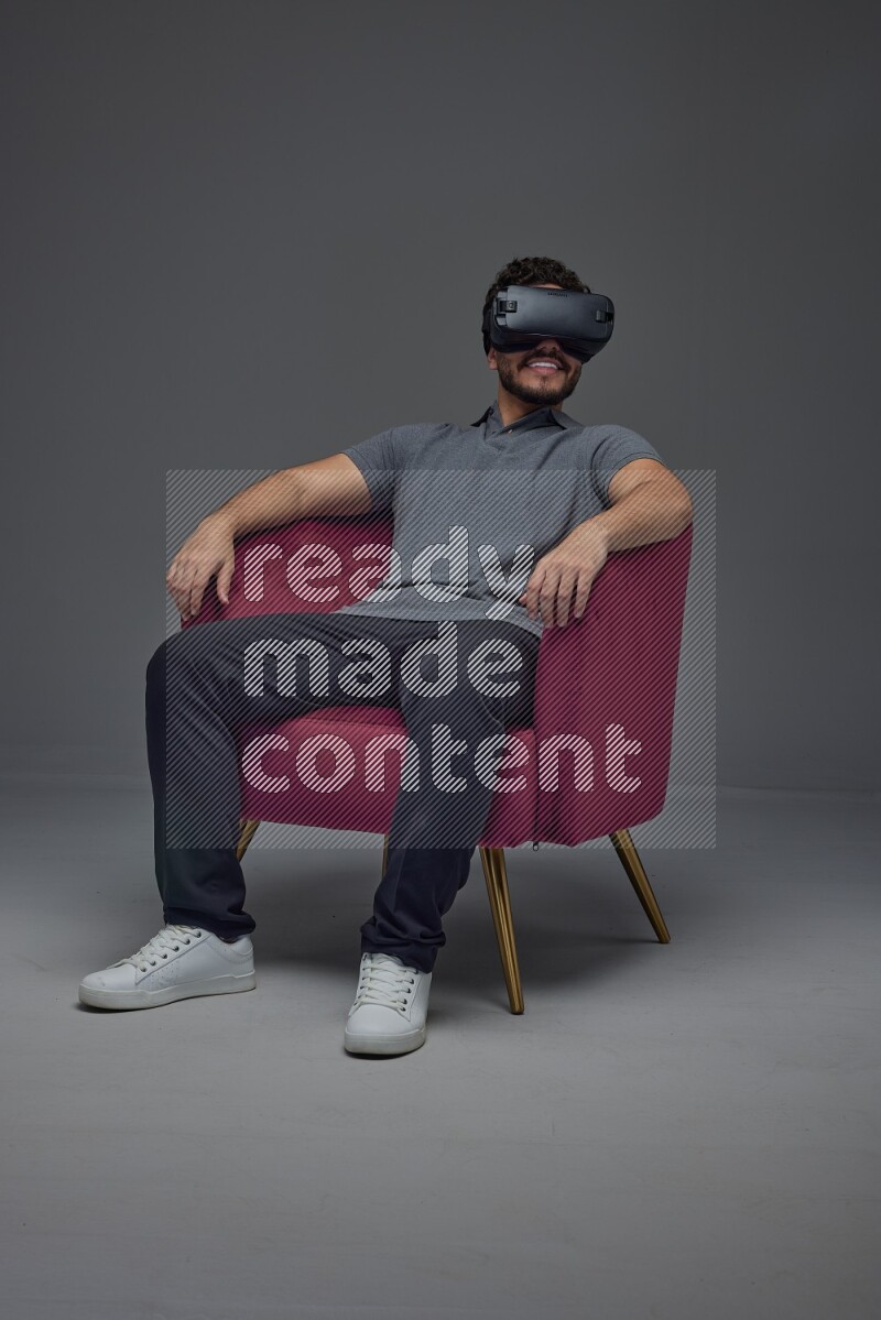 A man wearing casual and wearing VR while sitting on a burgundy chair eye level on a gray background