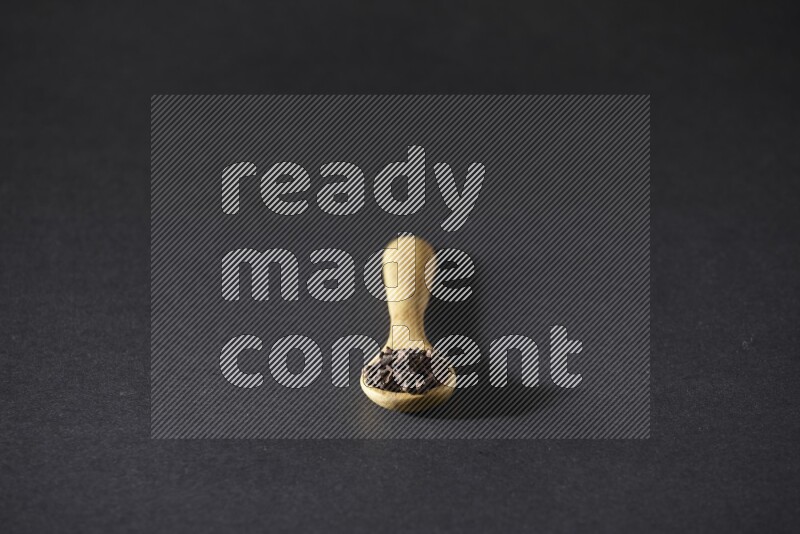 A wooden spoon full of cloves on a black flooring