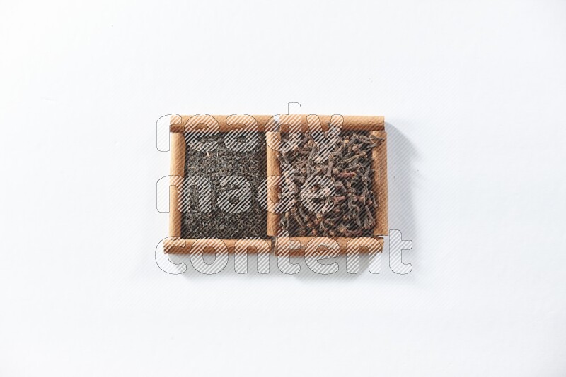 مربعان من أعواد القرفة ممتلئان بالشاي الأسود وحبوب القرنفل علي خلفية بيضاء